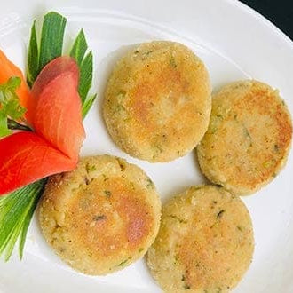 Golden, crispy potato kababs (Aloo Tikki) served on a plate, garnished with fresh coriander and a side of tangy chutney. The kababs have a slightly crunchy exterior, with a soft, spiced potato filling peeking through. The vibrant green chutney adds color and flavor contrast to the warm, savory kababs.